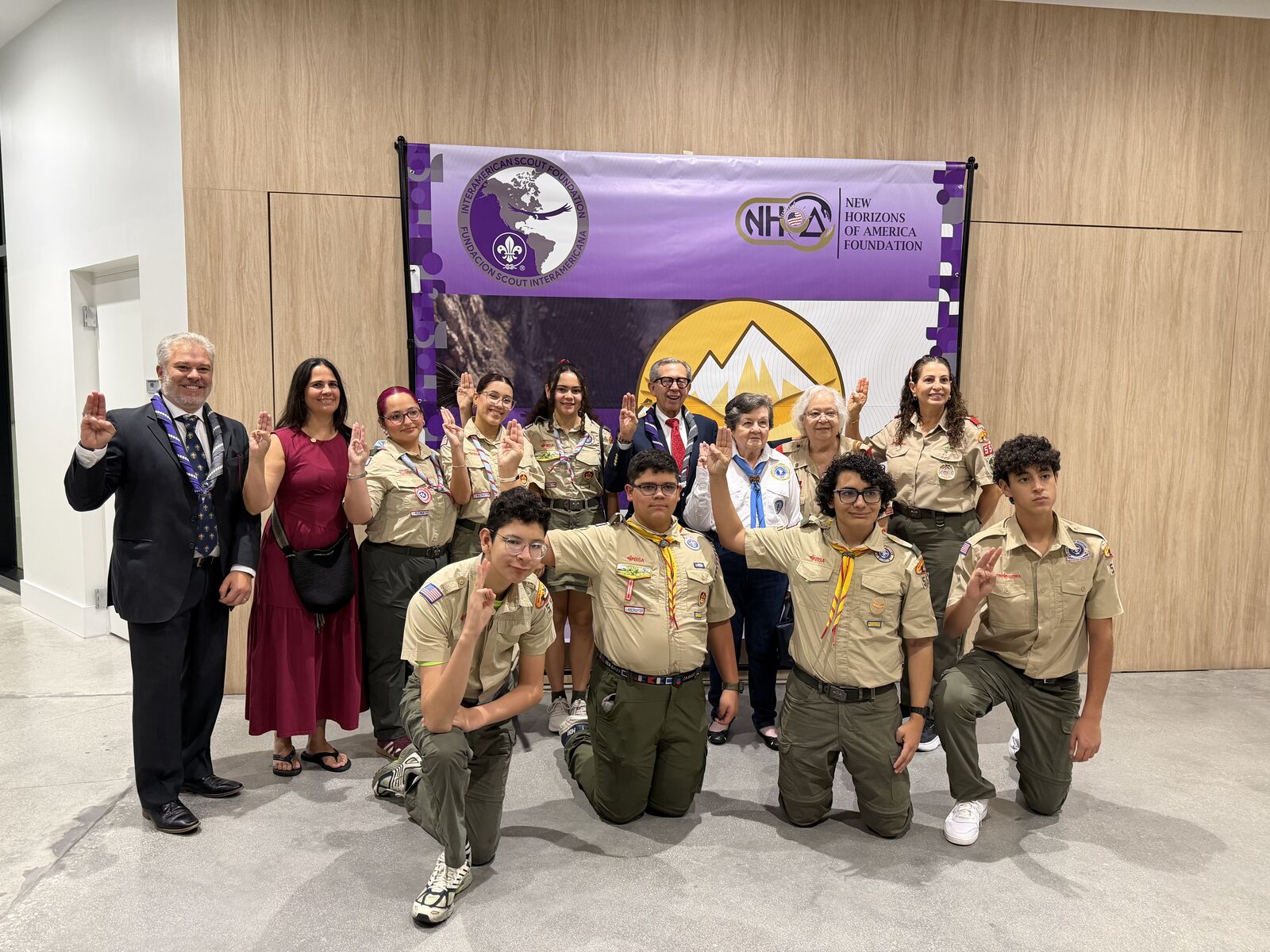 Supporters and young Scouts in uniform in front of the Interamerican Scout Foundation and New Horizons of America Foundation banner at the Christmas Night of Giving in Doral